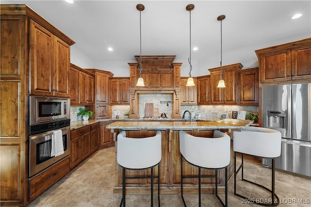 kitchen featuring backsplash, light stone countertops, a center island with sink, a breakfast bar area, and appliances with stainless steel finishes