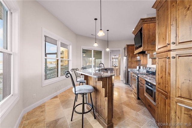 kitchen with baseboards, a kitchen island with sink, stainless steel appliances, a kitchen breakfast bar, and decorative light fixtures