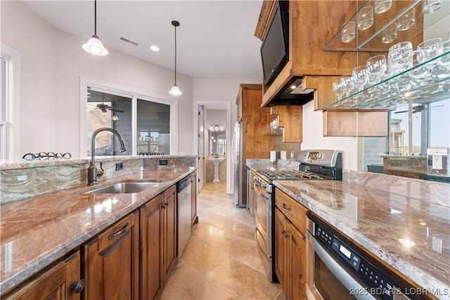 kitchen featuring brown cabinetry, a ceiling fan, a sink, appliances with stainless steel finishes, and pendant lighting