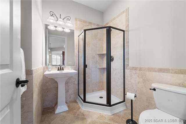 full bathroom featuring tile walls, toilet, a shower stall, and a sink