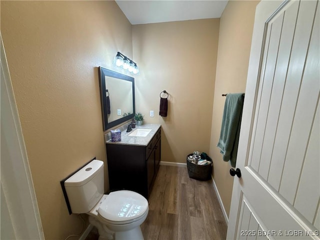 half bathroom featuring baseboards, vanity, toilet, and wood finished floors