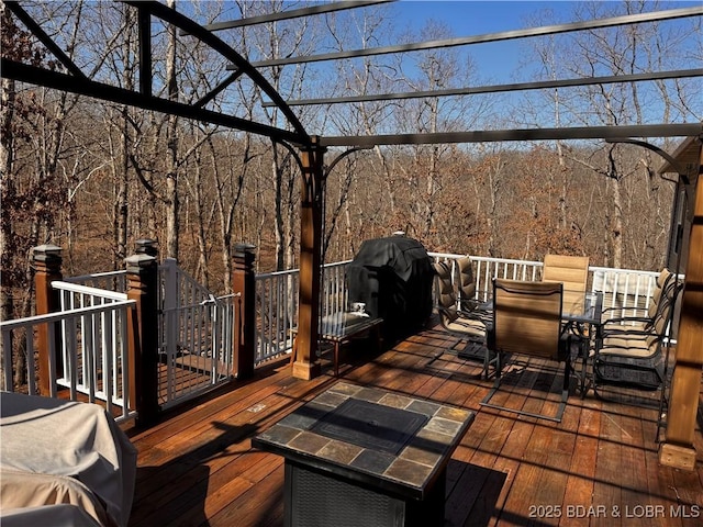 deck with outdoor dining space, grilling area, and a wooded view