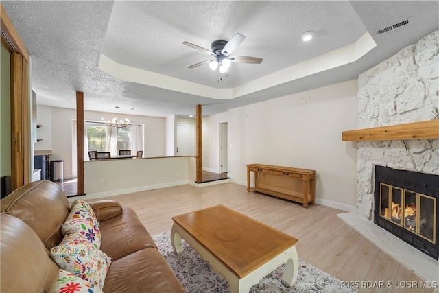 living area featuring a tray ceiling, visible vents, a fireplace, and light wood finished floors