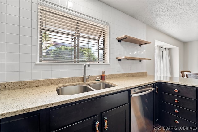 kitchen with light stone counters, dark cabinets, a sink, a textured ceiling, and stainless steel dishwasher