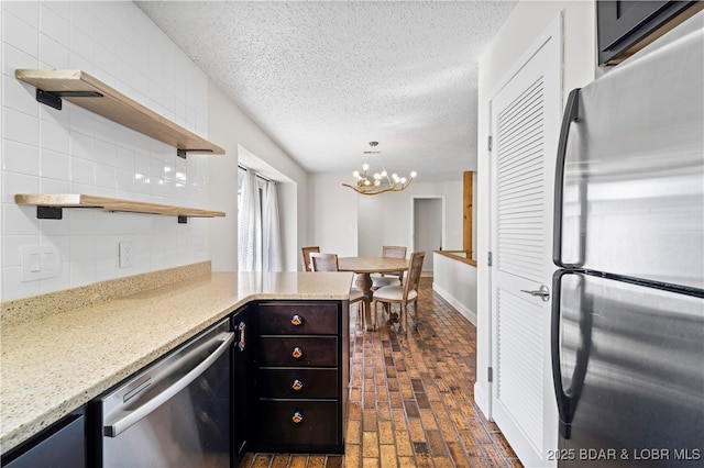 kitchen with brick floor, open shelves, tasteful backsplash, appliances with stainless steel finishes, and a textured ceiling