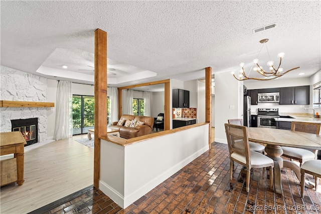 kitchen with appliances with stainless steel finishes, a tray ceiling, open floor plan, and a fireplace