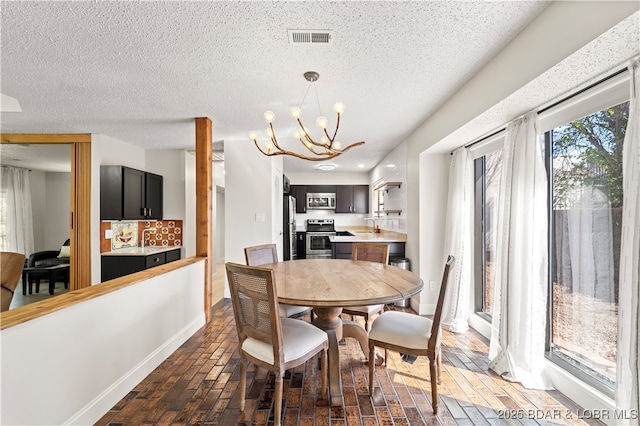 dining area with a textured ceiling, brick floor, a notable chandelier, visible vents, and baseboards