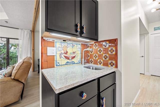 kitchen with a textured ceiling, light stone counters, light wood-type flooring, and a sink