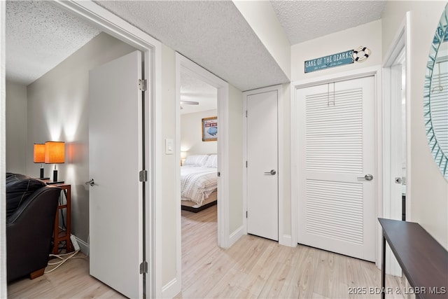 hallway with a textured ceiling, light wood-type flooring, and baseboards