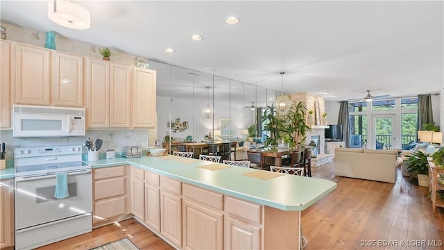 kitchen with white appliances, a peninsula, light wood-style flooring, light countertops, and open floor plan