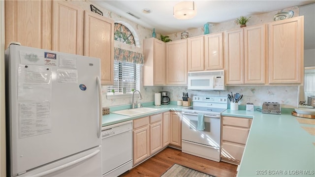 kitchen featuring white appliances, light brown cabinets, light countertops, and a sink