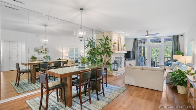 dining area featuring visible vents, a stone fireplace, wood finished floors, and a ceiling fan