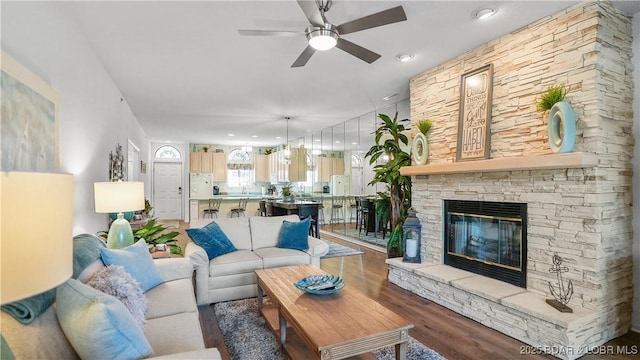 living area with a stone fireplace, a ceiling fan, and wood finished floors