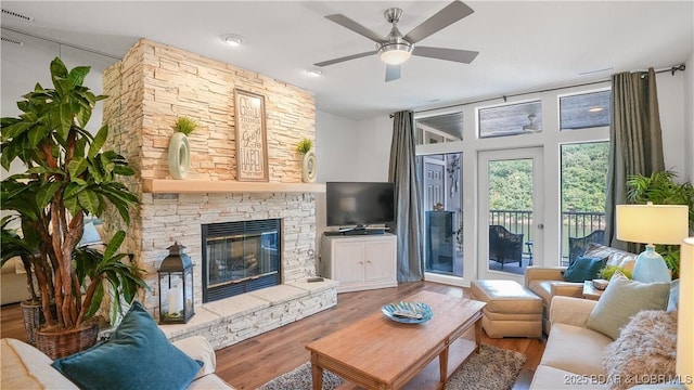 living area with a stone fireplace, wood finished floors, and a ceiling fan