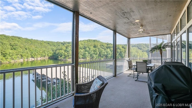 unfurnished sunroom with a view of trees, ceiling fan, and a water view