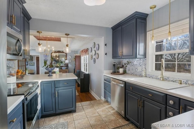 kitchen featuring a sink, stainless steel appliances, light countertops, decorative backsplash, and hanging light fixtures