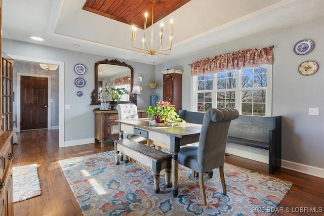 dining space featuring a raised ceiling, wood finished floors, baseboards, and a chandelier