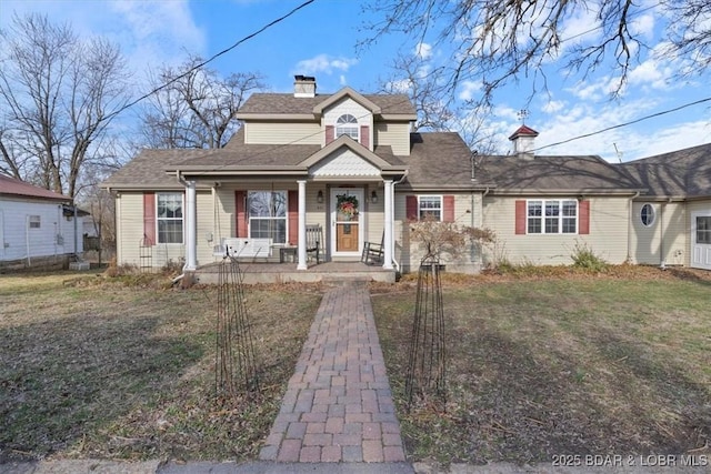 view of front facade with a shingled roof, a porch, a front lawn, and a chimney