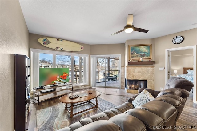 living area with a tiled fireplace, wood finished floors, a textured wall, and ceiling fan