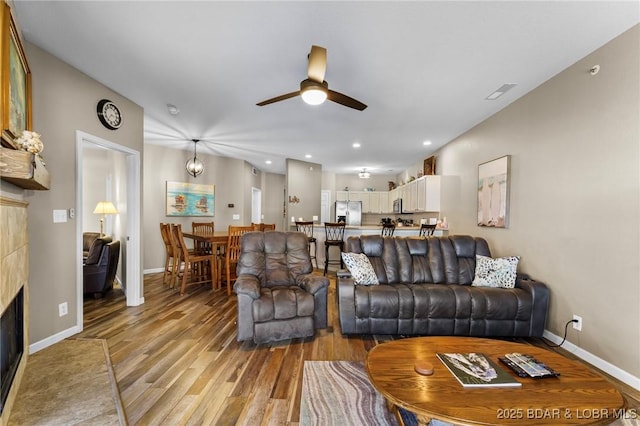 living area with ceiling fan, baseboards, light wood-style flooring, and a fireplace