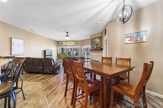 dining space featuring visible vents, baseboards, light wood-type flooring, ceiling fan with notable chandelier, and a tile fireplace