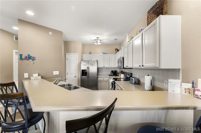 kitchen featuring a peninsula, a sink, light countertops, appliances with stainless steel finishes, and backsplash