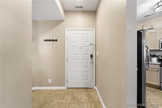 doorway to outside featuring light tile patterned flooring, baseboards, visible vents, and a textured wall