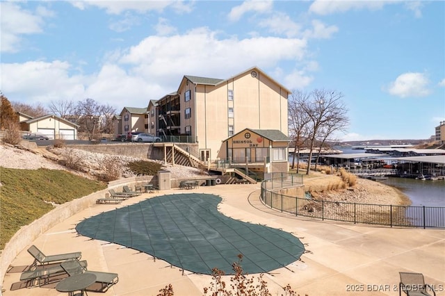 community pool with a water view, a patio, and fence