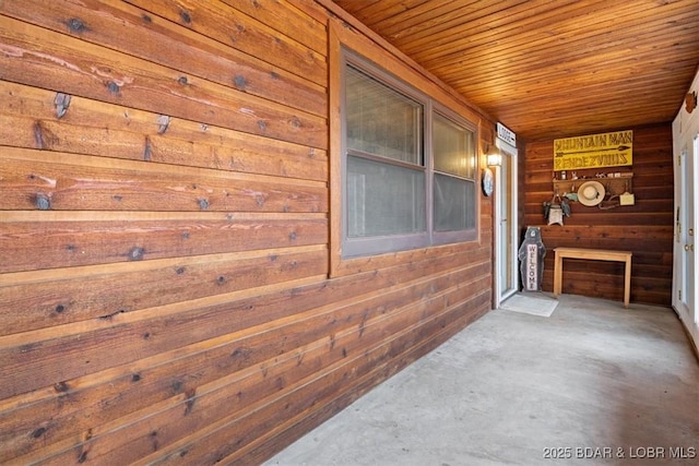 corridor with wooden walls, wooden ceiling, and concrete flooring