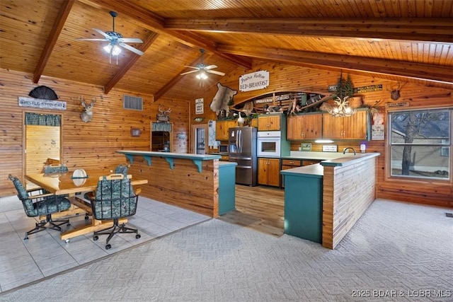 kitchen featuring oven, stainless steel fridge, a peninsula, brown cabinetry, and vaulted ceiling with beams