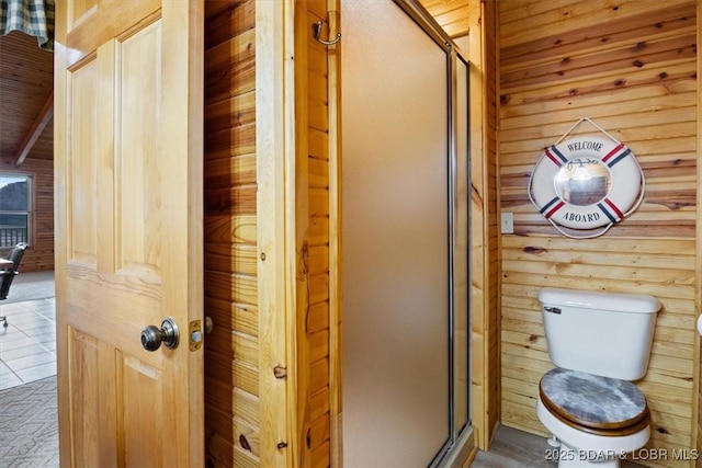 bathroom featuring toilet, a stall shower, and wood walls