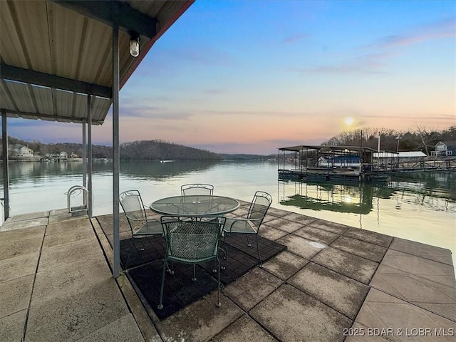 patio terrace at dusk featuring outdoor dining space, a dock, and a water view