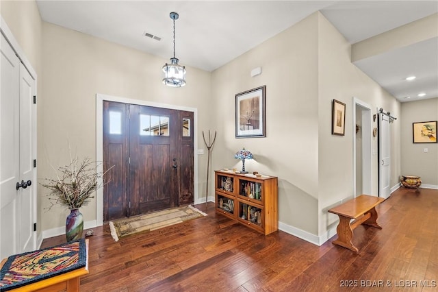 foyer entrance with visible vents, baseboards, a barn door, a notable chandelier, and wood-type flooring