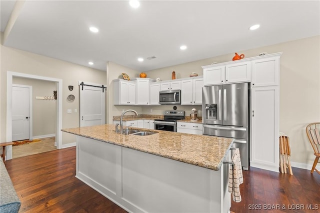 kitchen with a barn door, appliances with stainless steel finishes, dark wood-style floors, white cabinetry, and a sink