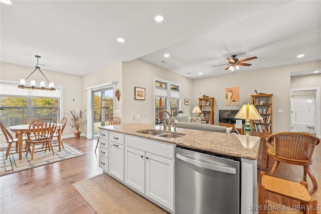 kitchen featuring white cabinetry, an island with sink, a sink, stainless steel dishwasher, and light wood-type flooring