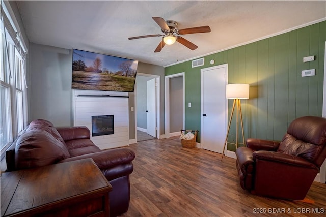 living area with visible vents, a ceiling fan, wood finished floors, a fireplace, and crown molding