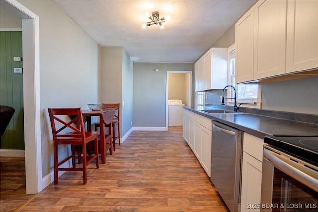 kitchen with light wood-style flooring, a sink, white cabinets, appliances with stainless steel finishes, and dark countertops