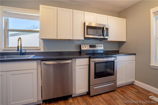 kitchen with dark countertops, visible vents, appliances with stainless steel finishes, white cabinets, and a sink