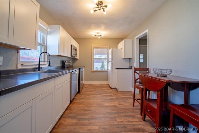 kitchen featuring wood finished floors, a sink, white cabinets, appliances with stainless steel finishes, and dark countertops