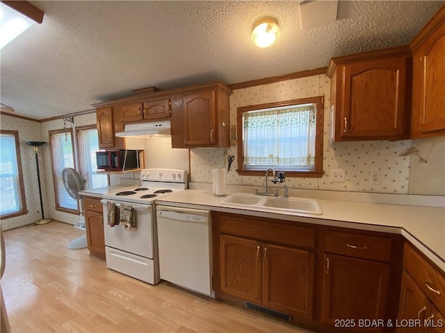 kitchen featuring under cabinet range hood, white appliances, wallpapered walls, and a sink