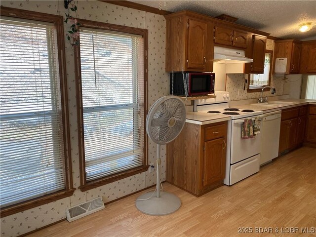 kitchen with white appliances, visible vents, wallpapered walls, a sink, and under cabinet range hood