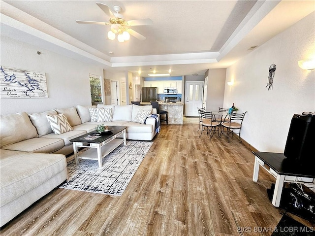 living room with plenty of natural light, a ceiling fan, light wood-type flooring, and a tray ceiling