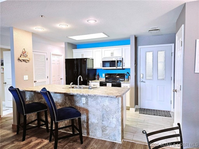 kitchen with black appliances, a kitchen bar, light wood-style floors, white cabinetry, and a sink