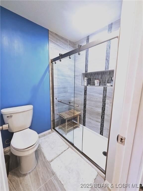 bathroom with baseboards, toilet, and a stall shower