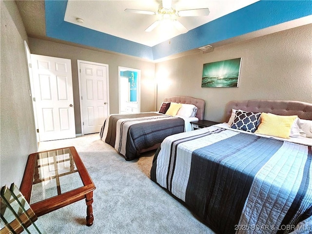 bedroom with a raised ceiling, carpet, ceiling fan, and a textured wall