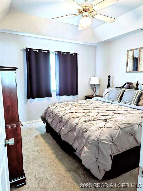 carpeted bedroom with baseboards, a raised ceiling, and a ceiling fan