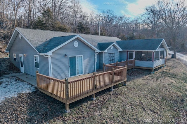 rear view of property featuring a wooden deck, a shingled roof, and a sunroom