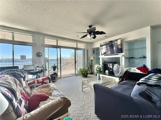 living area with carpet floors, plenty of natural light, a glass covered fireplace, and ceiling fan