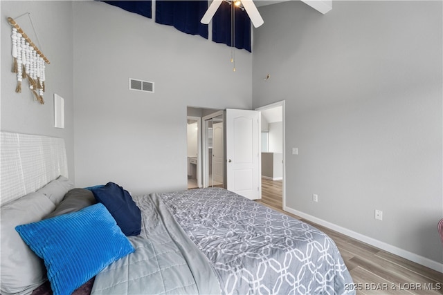bedroom with a high ceiling, wood finished floors, baseboards, ceiling fan, and ensuite bath