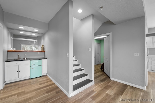indoor wet bar featuring light wood-type flooring, baseboards, stairs, recessed lighting, and refrigerator